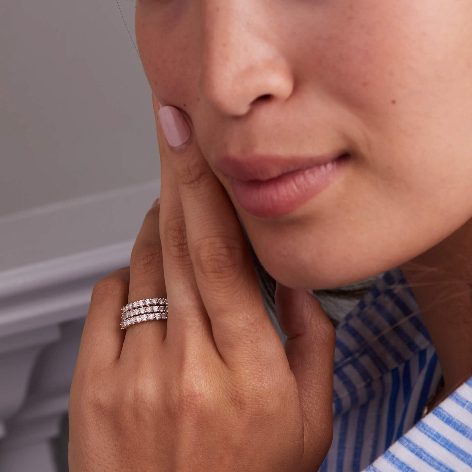 A woman wearing three personalized Rosecliff stackable rings in 14k yellow gold, each adorned with eleven 2mm faceted round-cut white topaz gems, elegantly displayed on her hand.