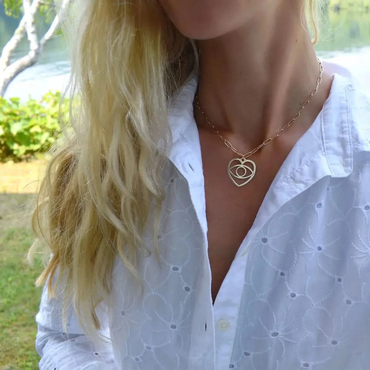 Yellow gold large Evil Eye Heart Pendant styled with a white blouse, highlighting its lightweight, statement look.