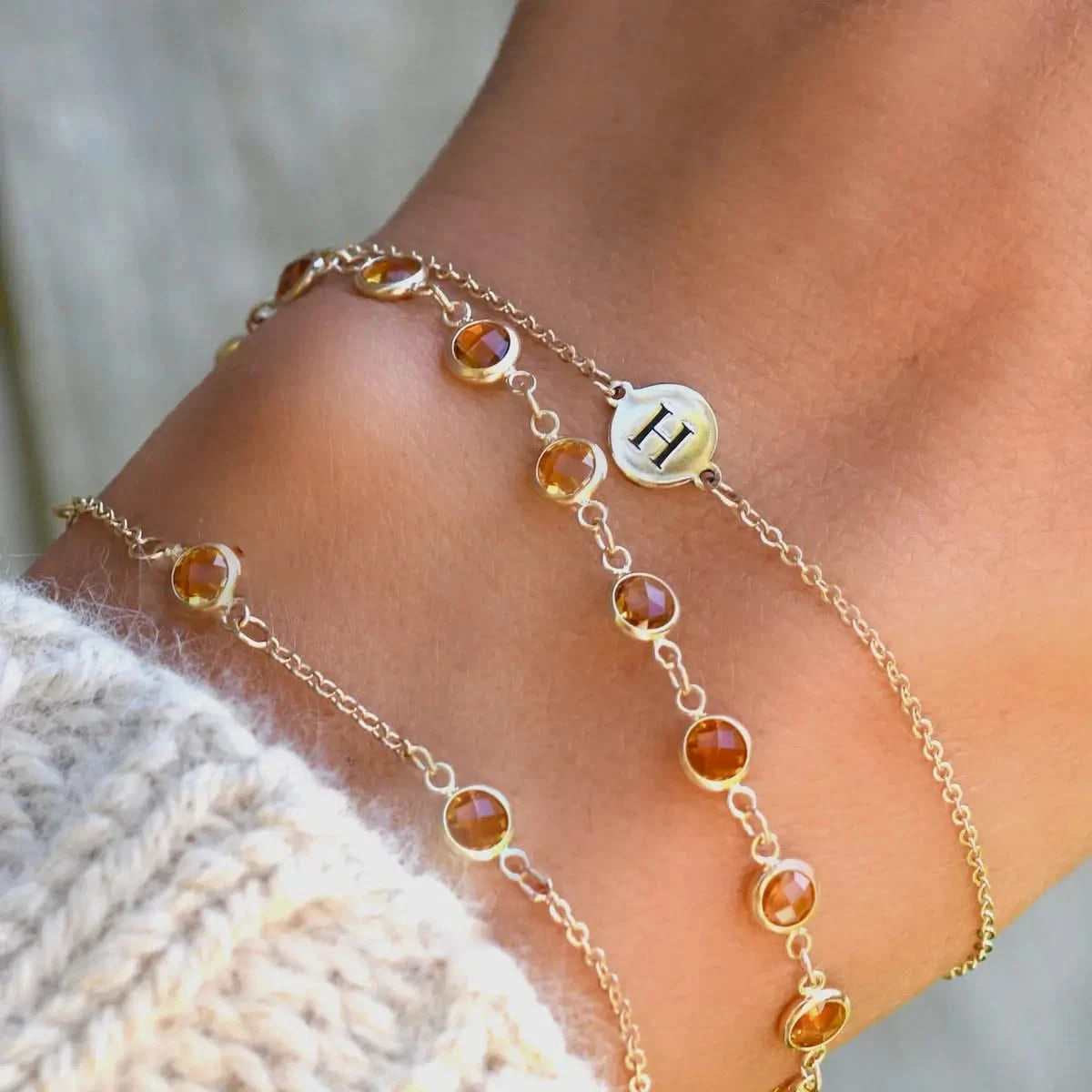 Close-up of layered bracelets including Newport Citrine Bracelet and engraved initial charm in 14k gold.