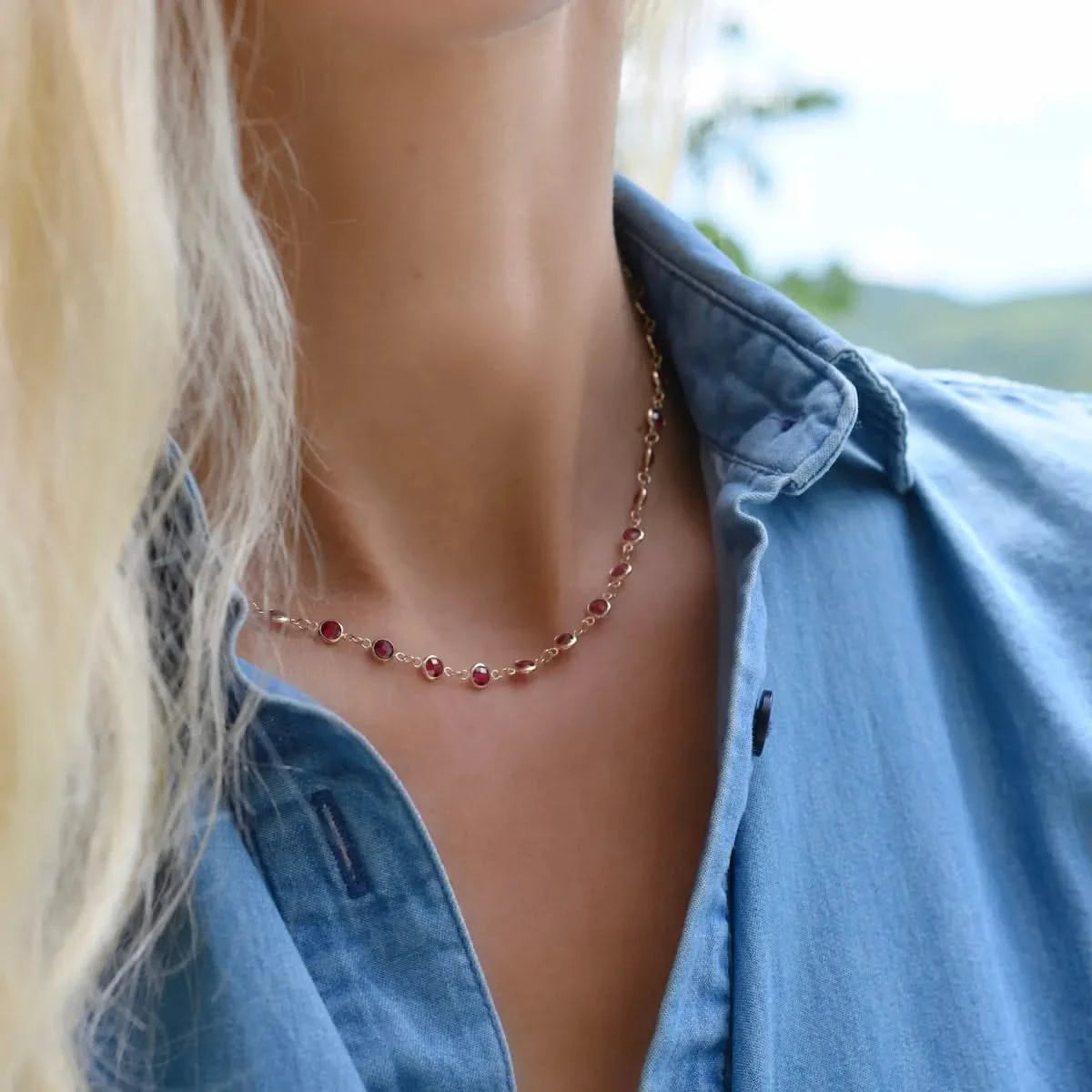 Woman wearing a Newport necklace featuring 4 mm briolette cut rubies bezel set in 14k yellow gold
