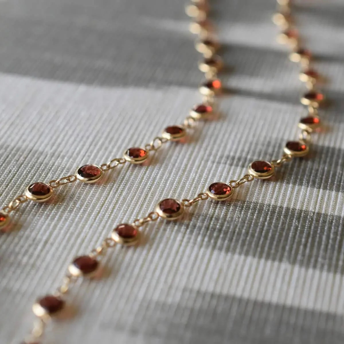 Close-up of garnet stones on Newport necklace in 14k gold, laid on striped fabric.