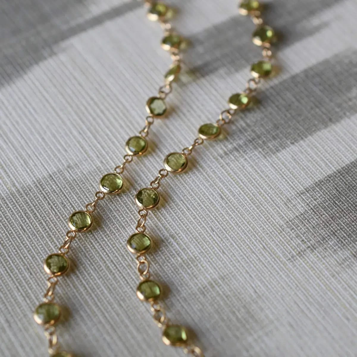 Close-up flatlay of the Newport Peridot Necklace in 14k gold, showcasing round bezel-set green Peridot gemstones.