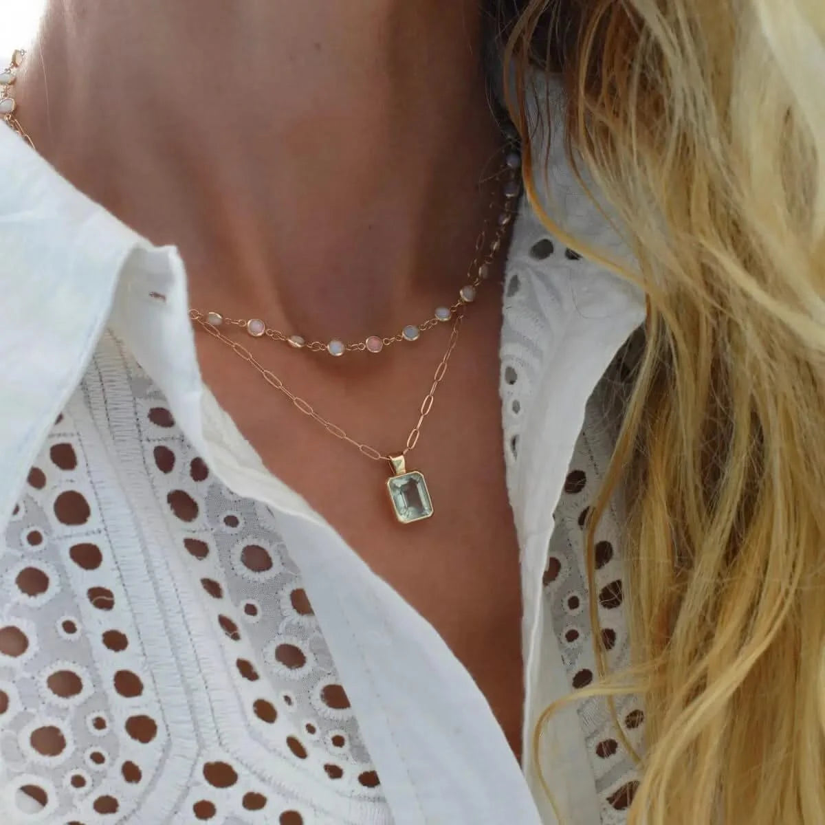 Opal necklace worn with a green amethyst pendant, styled with a white eyelet blouse and blonde hair partially in frame.