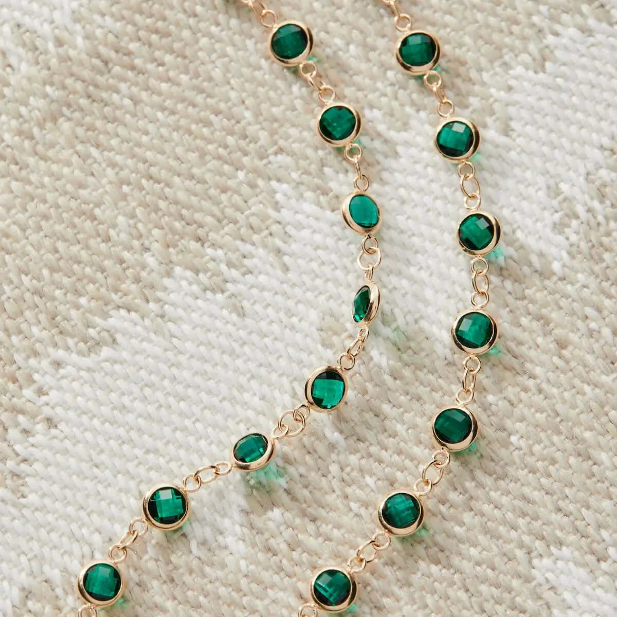 Newport Emerald Necklace paired with a gold initial charm necklace, laid flat on a pale pink background.