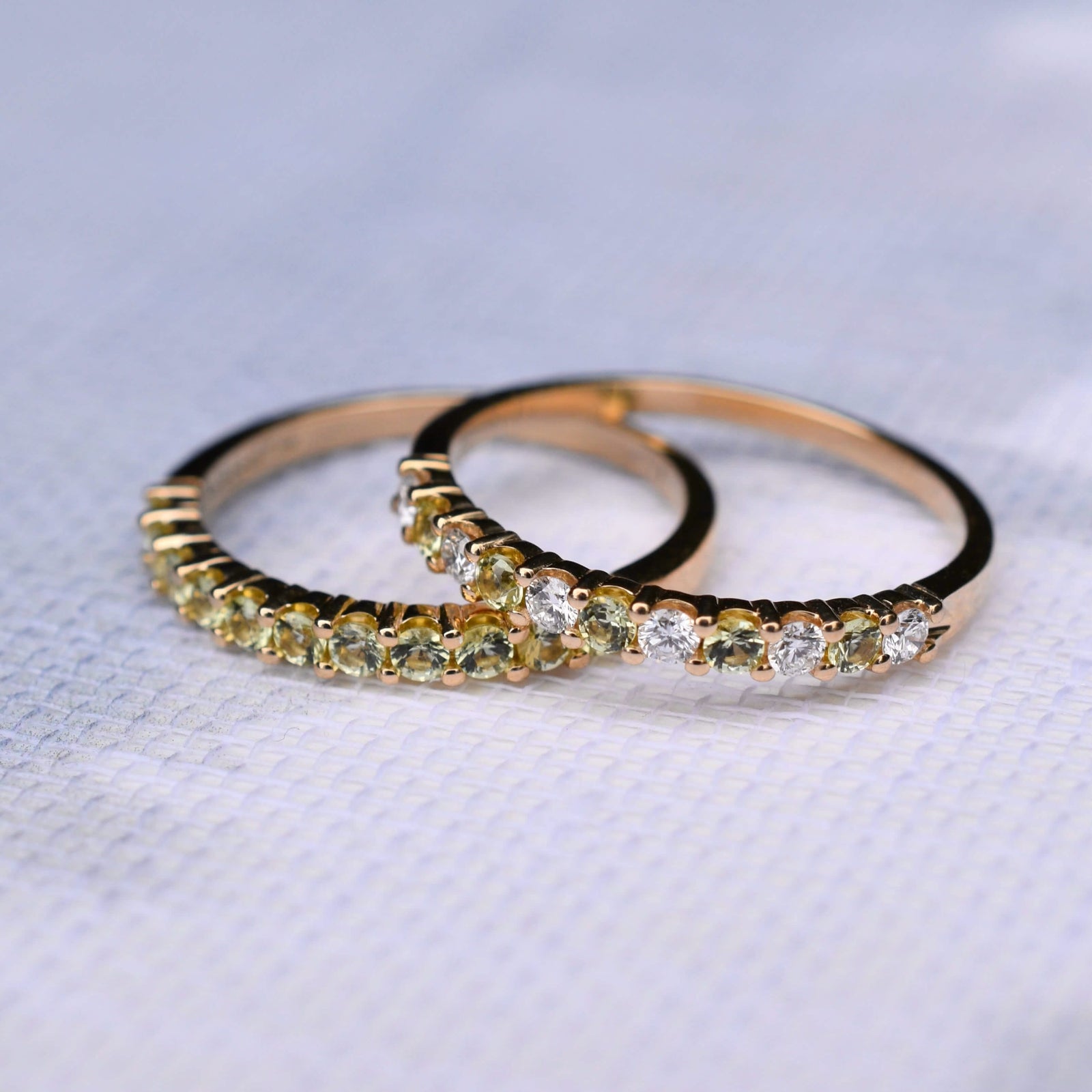 Close-up of two Rosecliff Peridot Stackable Rings in 14k gold, one featuring eleven 2 mm faceted round-cut, prong-set Peridots, and the other alternating Peridots and Diamonds.