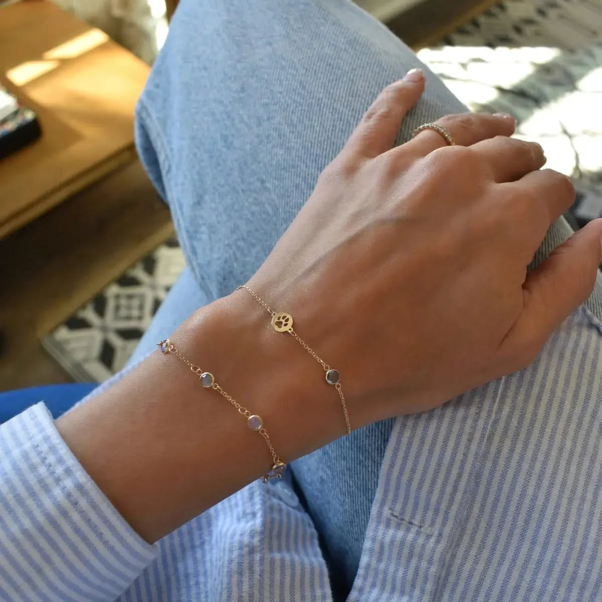 The Paw & Petite Birthstone Bracelet in 14k gold is worn on a woman’s wrist, layered with a bezel-set multi-birthstone bracelet.