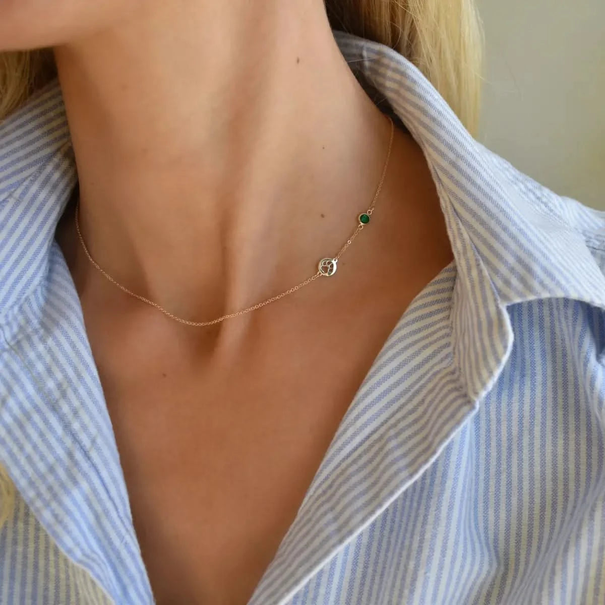 A woman is shown wearing the 14k yellow gold paw & birthstone necklace near the collarbone with a blue-striped blouse.