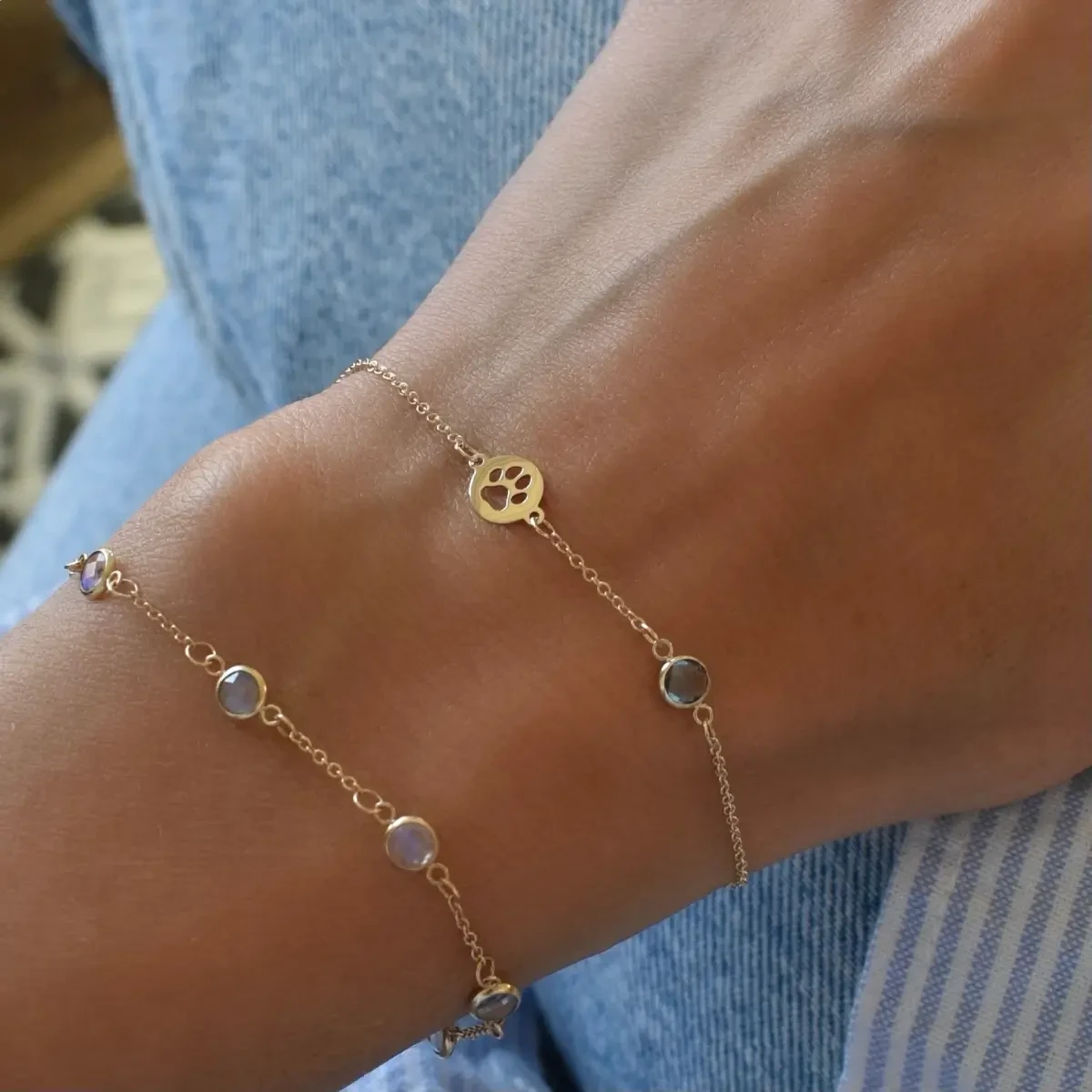 A close-up of a woman’s wrist highlights the Paw & Petite Birthstone Bracelet with a white gemstone and 1/4" paw charm cutout in gold.