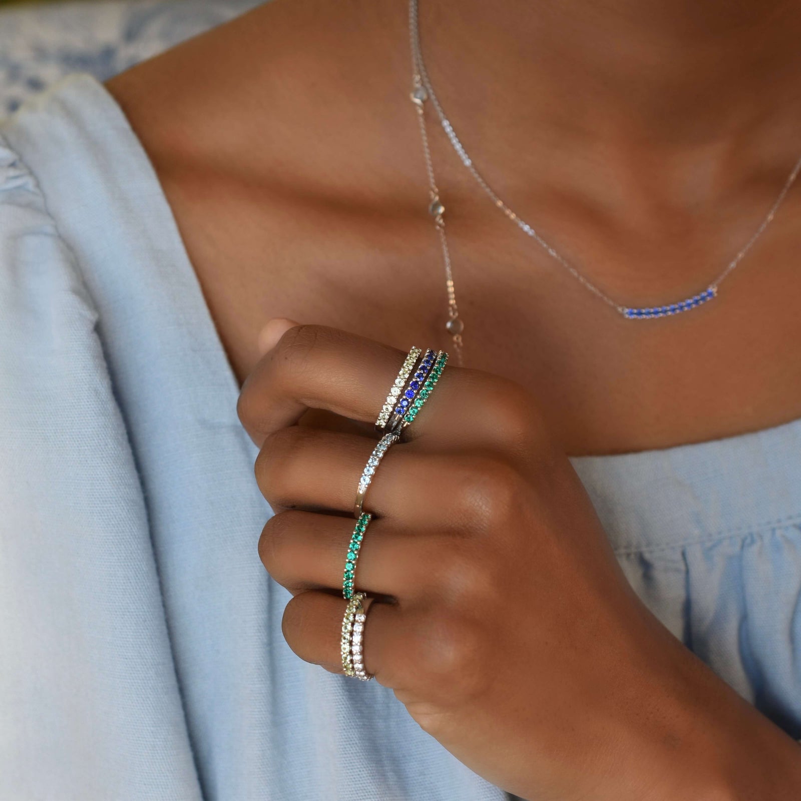 A woman wearing seven personalized Rosecliff stackable rings in 14k yellow gold, each adorned with eleven 2mm faceted round-cut gems, elegantly displayed on her hand.