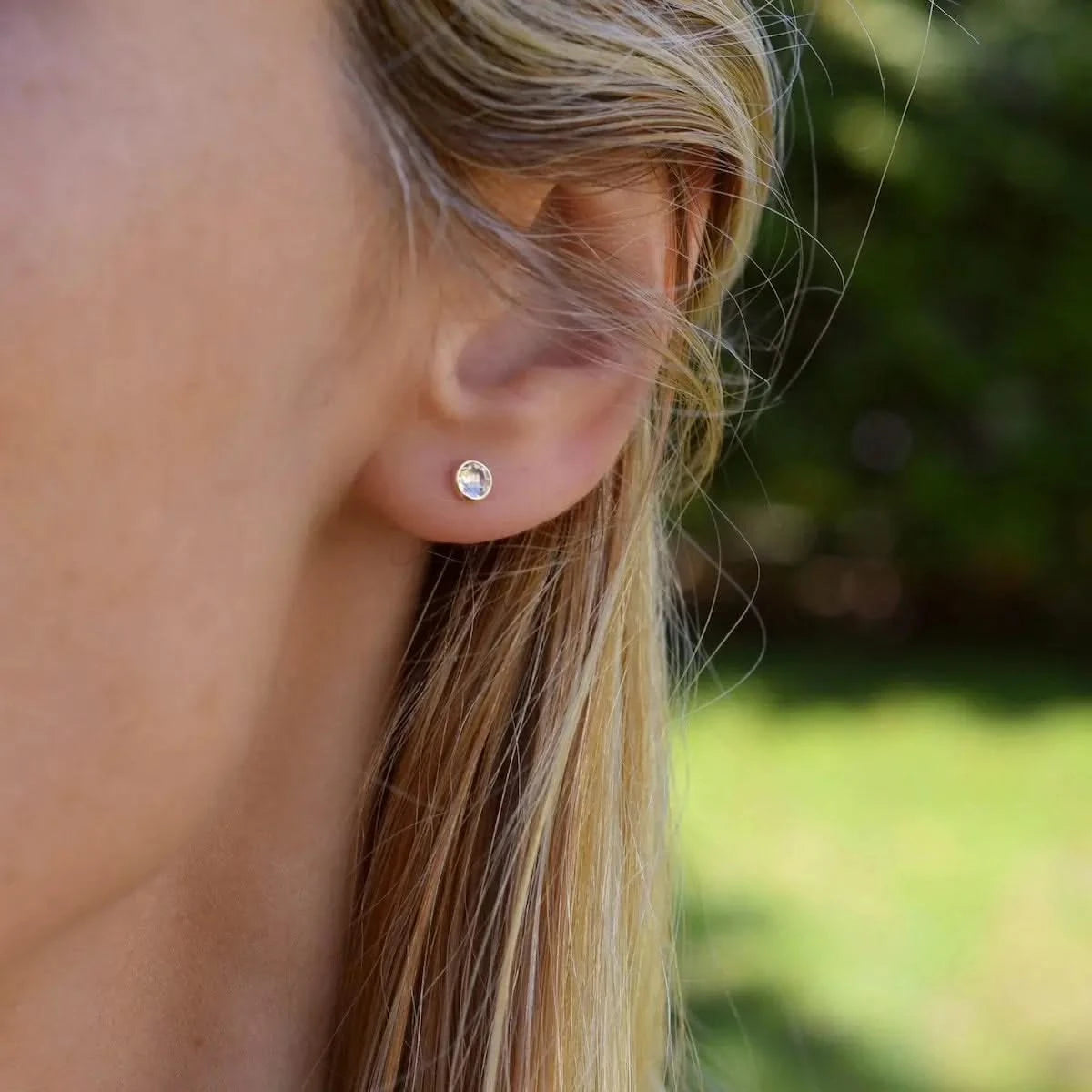 Woman wearing a Birthstone Stud Earring featuring a 4 mm briolette cut White Topaz bezel set in 14k yellow gold