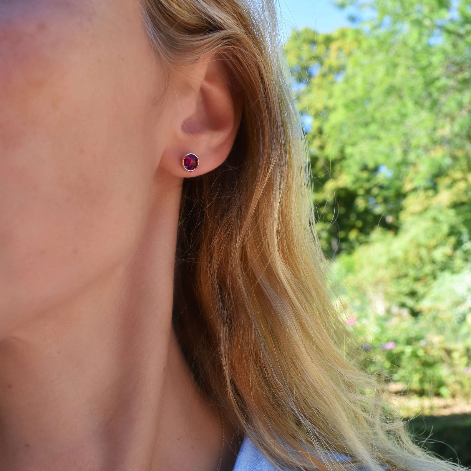 Woman wearing a pair of 14k yellow gold Grand stud earrings each featuring one 6 mm briolette cut Ruby