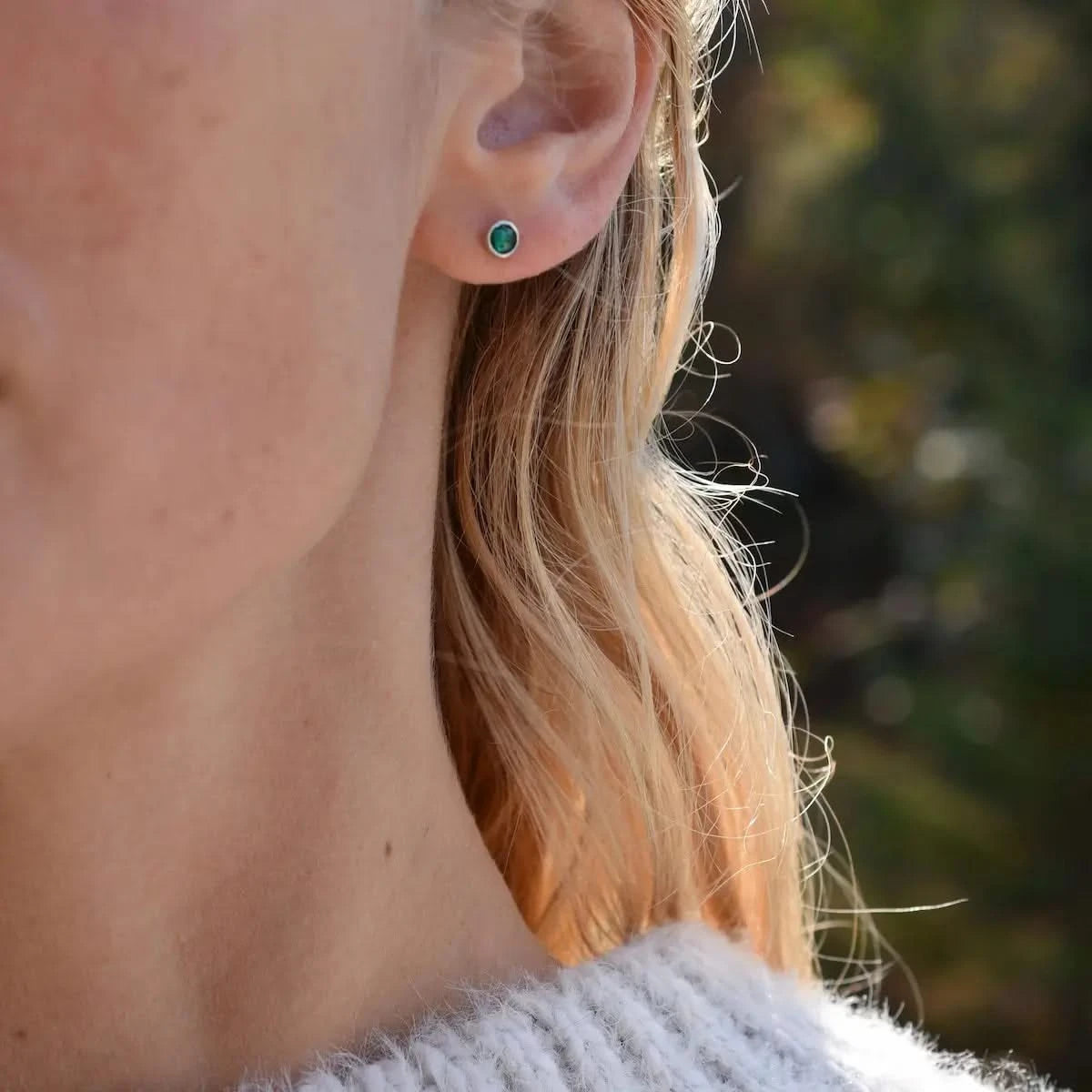 Woman wearing a Birthstone Stud Earring featuring a 4 mm briolette cut Emerald bezel set in 14k white gold