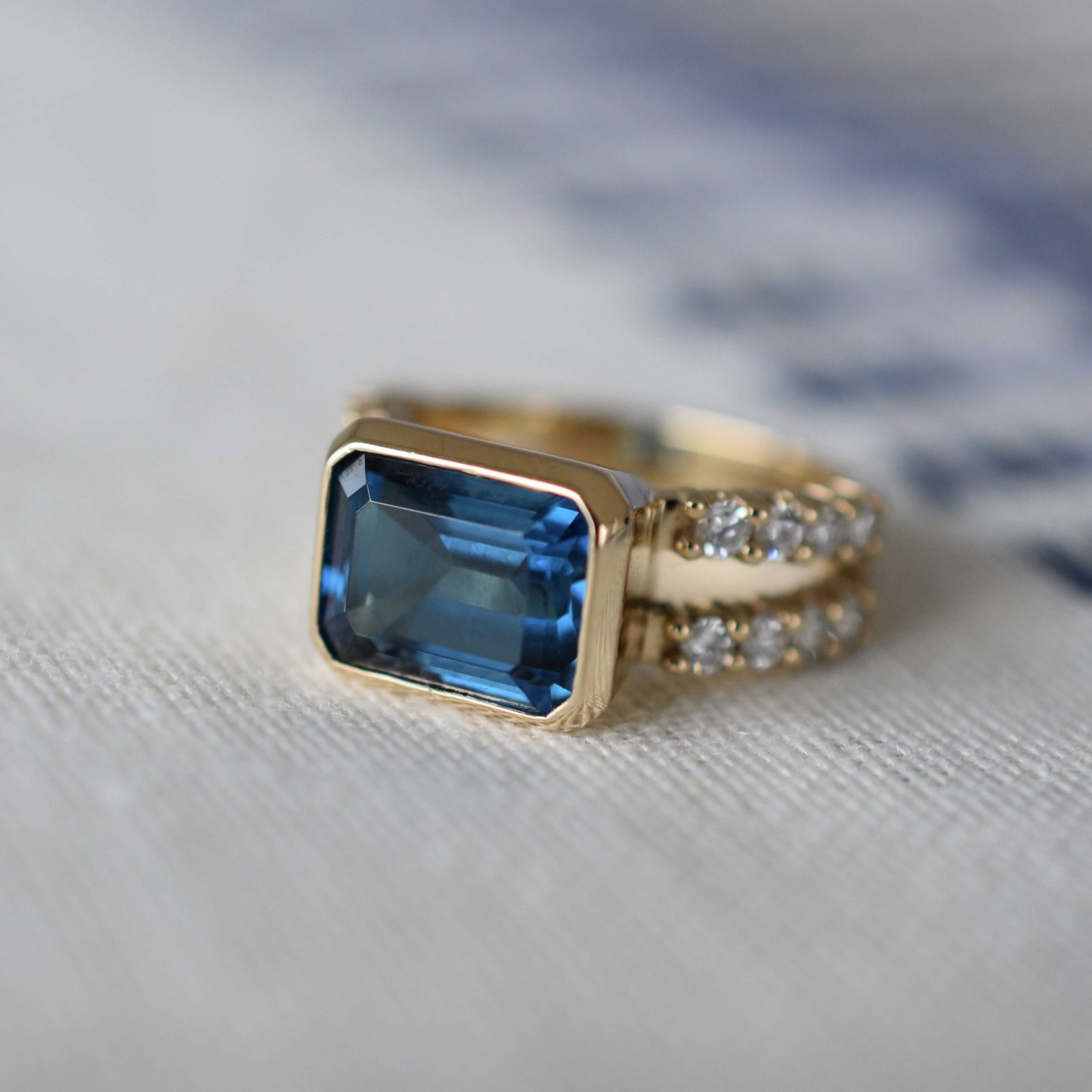 Aspect view of a Warren Horizontal Atlantic Blue Topaz Ring with Diamonds, featuring an 8 x 10mm Atlantic Blue Topaz and 16 prong-set diamonds in 14k yellow gold.