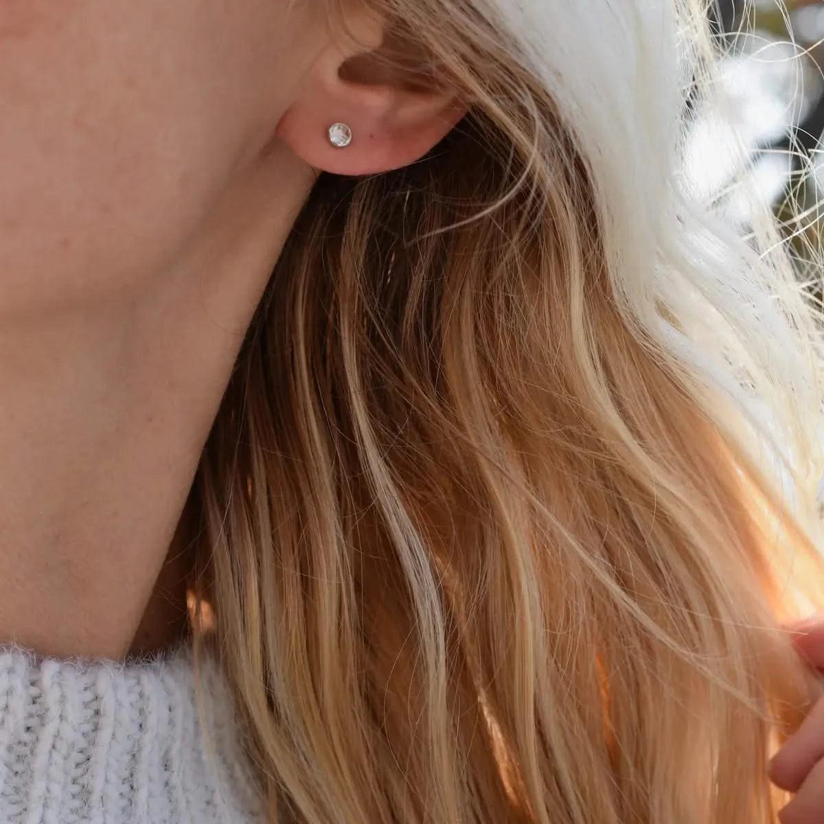 Woman wearing a Birthstone Stud Earring featuring a 4 mm briolette cut White Topaz bezel set in 14k white gold