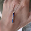 Woman holding a Providence vertical bar pendant featuring 6 petite Sapphire baguette stones set in 14k yellow gold