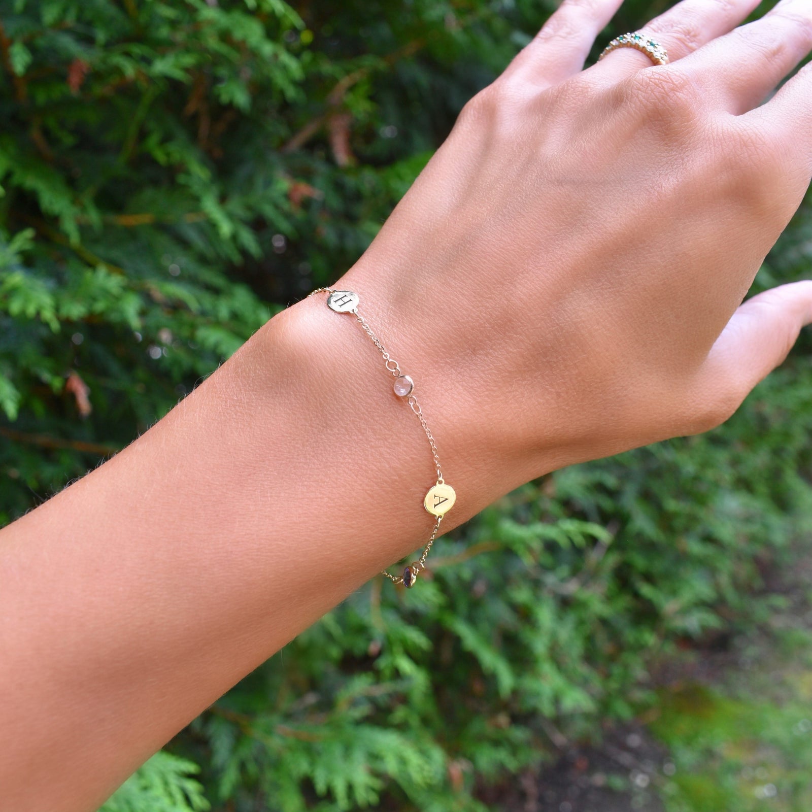 Woman wearing a 14k yellow gold Classic bracelet featuring birthstones and two 1/4” flat discs engraved with letters A & H
