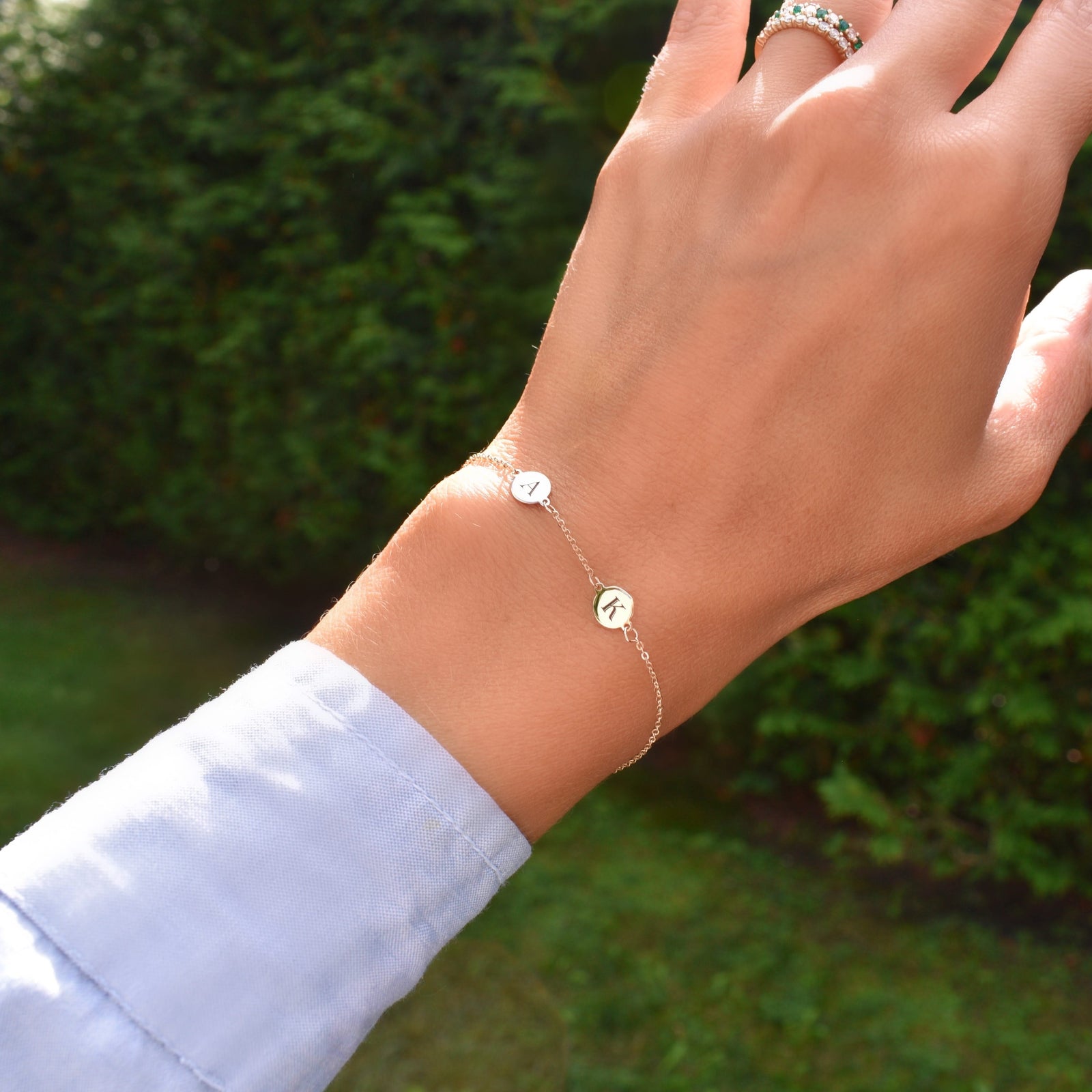 Woman wearing a 14k yellow gold cable chain bracelet featuring two 1/4” flat discs engraved with letters A and K