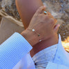 Woman wearing a 14k gold Classic bracelet featuring two birthstones and two 1/4” flat discs engraved with letters H & L