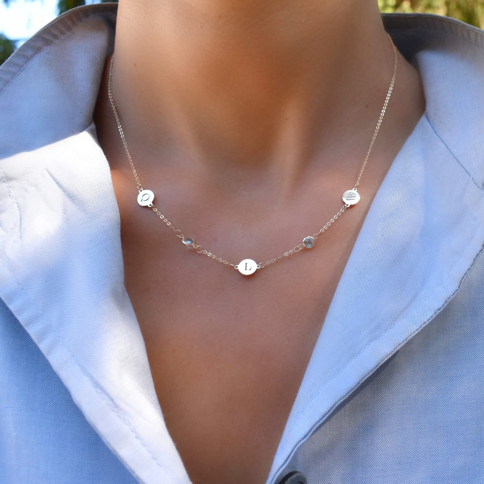 Woman with a 14k gold Classic necklace featuring two birthstones & three 1/4” flat letter-engraved discs