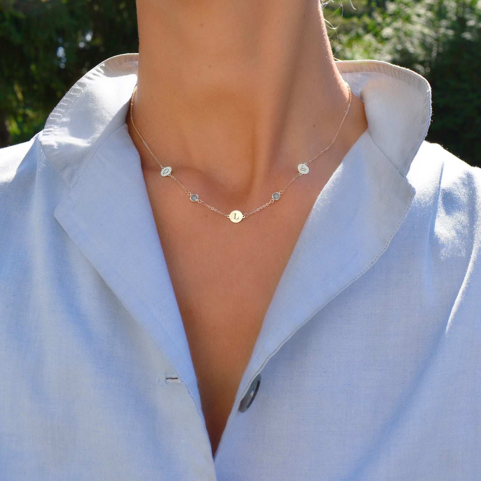 Woman wearing a 14k gold Classic necklace featuring two birthstones & three 1/4” flat letter-engraved discs