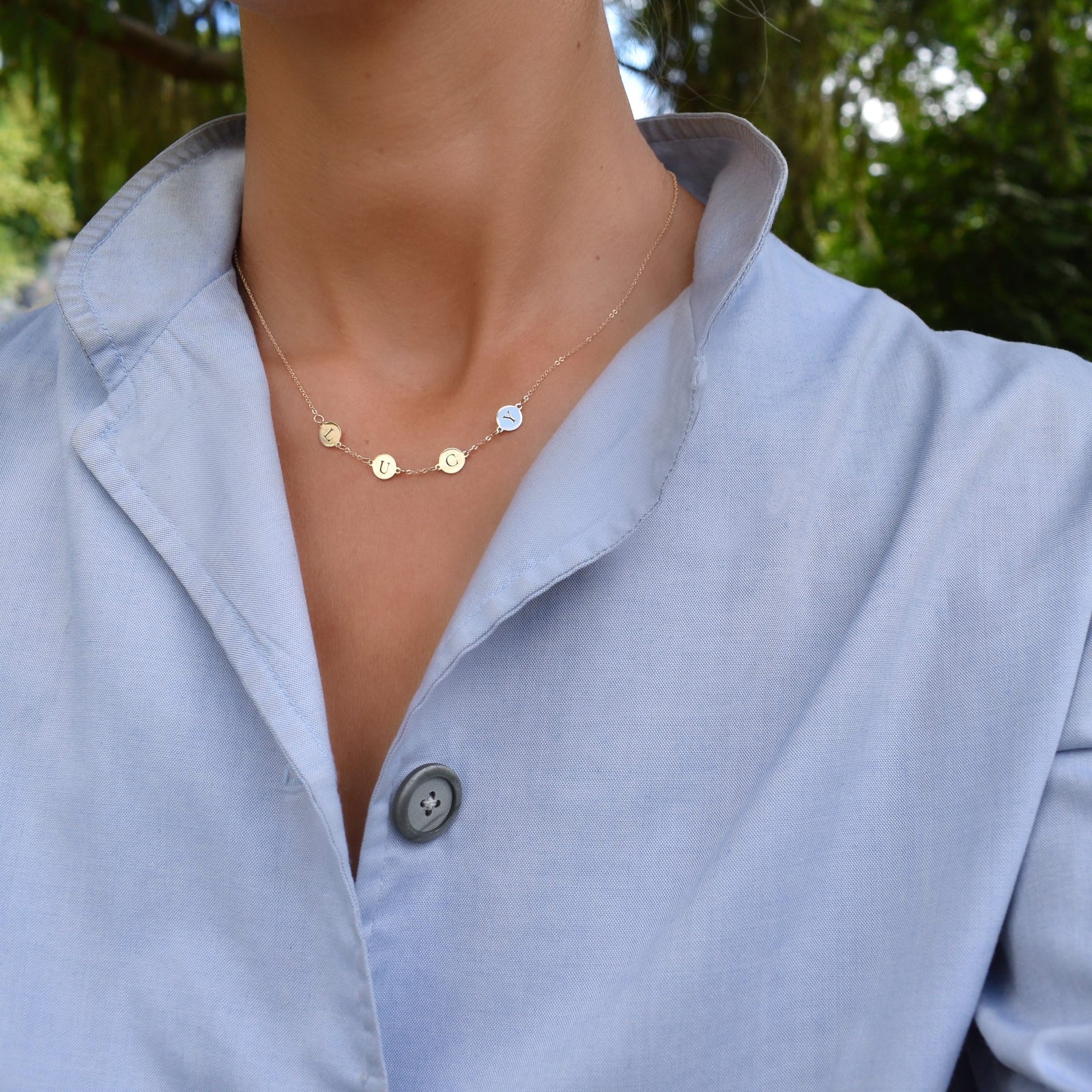 Woman wearing a 14k yellow gold cable chain necklace featuring four 1/4” flat discs engraved with the letters LUCY