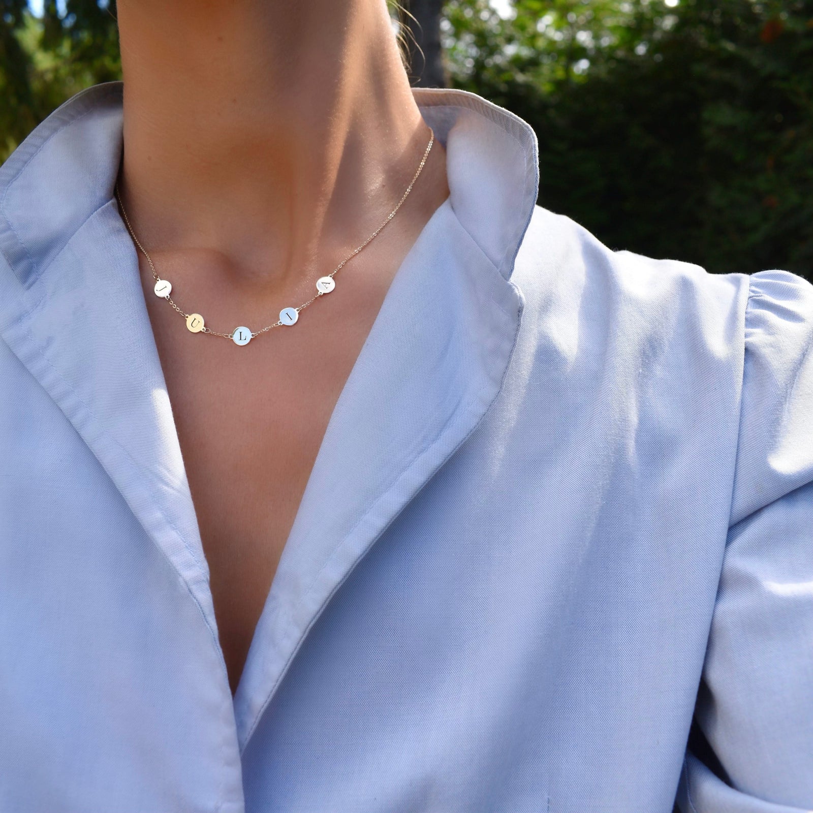 Woman wearing a 14k yellow gold cable chain necklace featuring five 1/4” flat discs engraved with the letters JULIA