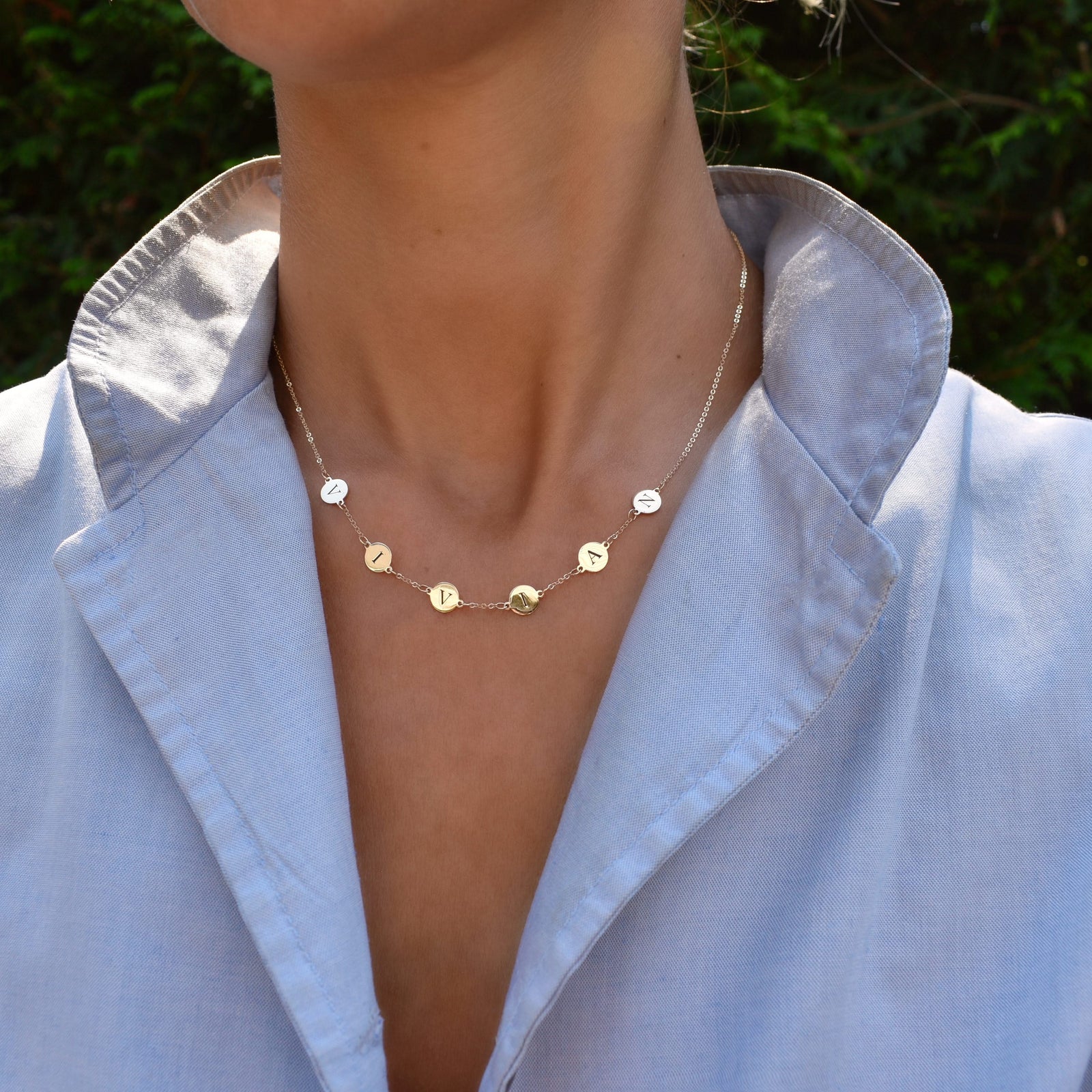 Woman wearing a 14k yellow gold cable chain necklace featuring six 1/4” flat engraved letter discs, spelling Vivian