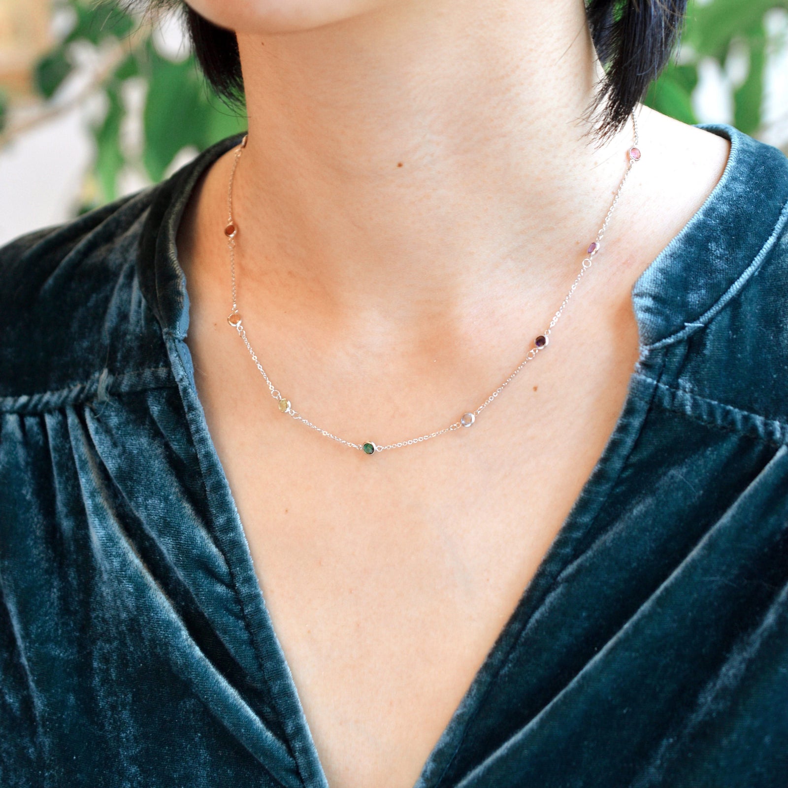 Woman wearing a Rainbow Bayberry 11 Birthstone necklace featuring 4 mm rainbow hued gemstones bezel set in 14k gold