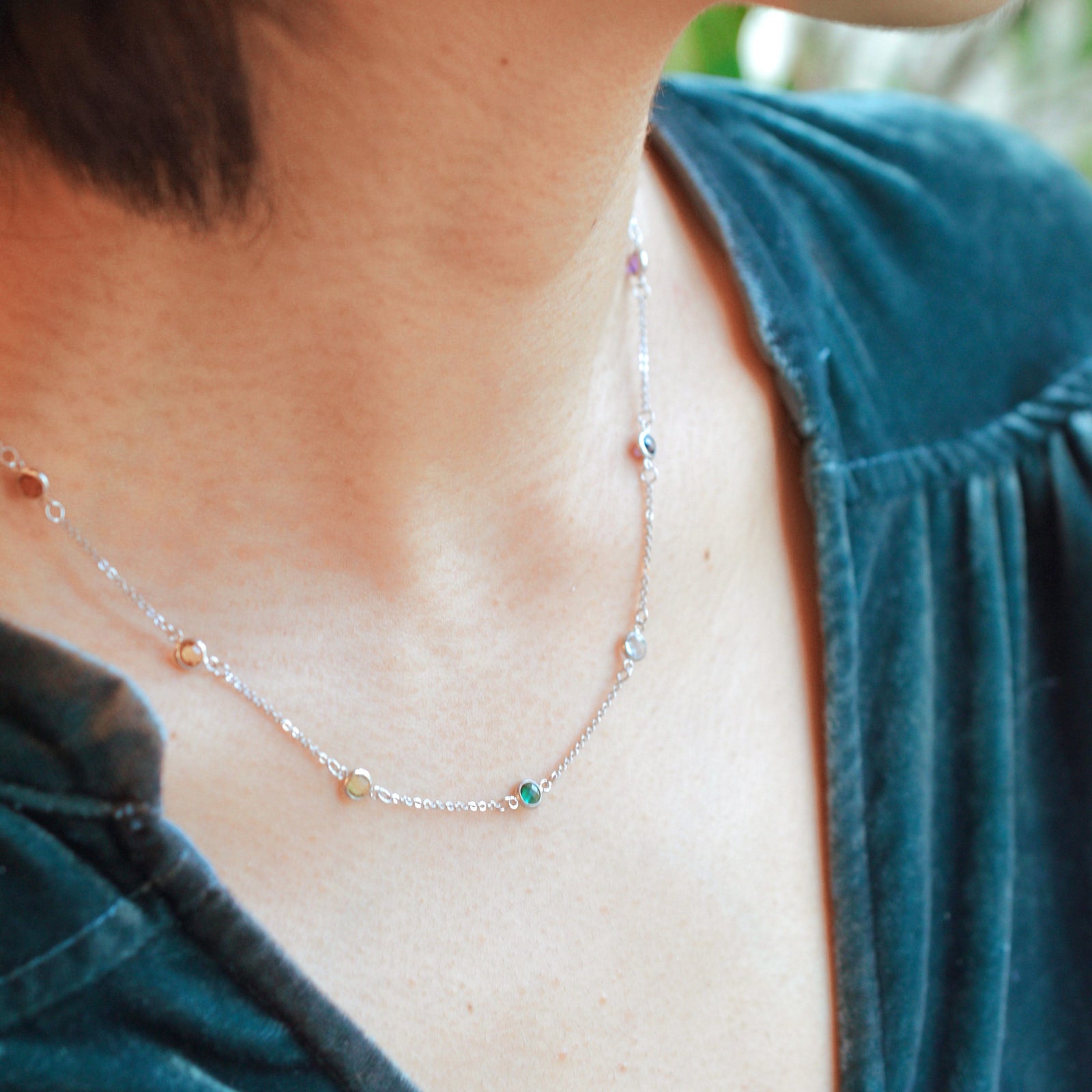 Woman with a Rainbow Bayberry 11 Birthstone necklace featuring 4 mm rainbow hued gemstones bezel set in 14k gold