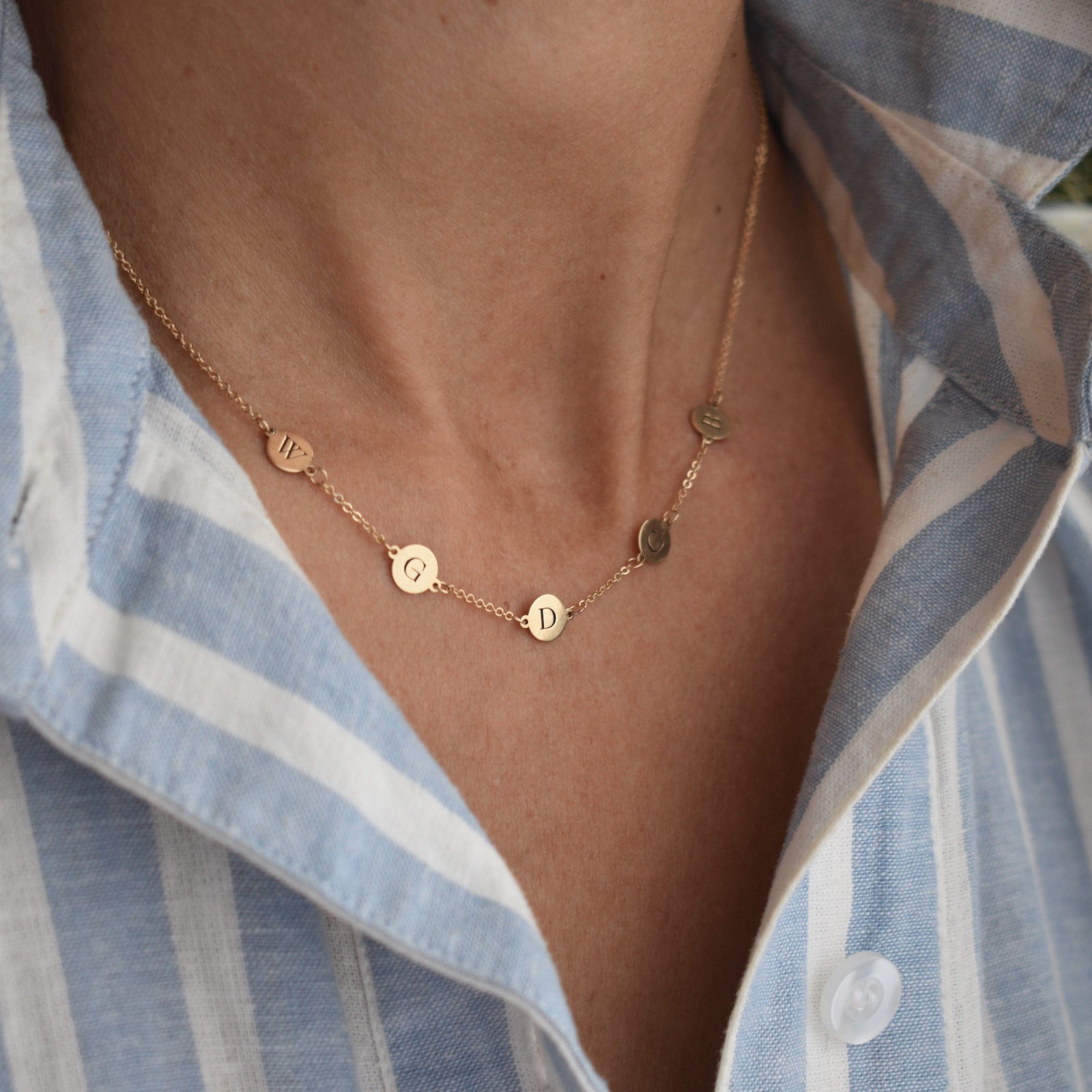 Woman wearing a 14k yellow gold cable chain necklace featuring five 1/4” flat discs engraved with letters