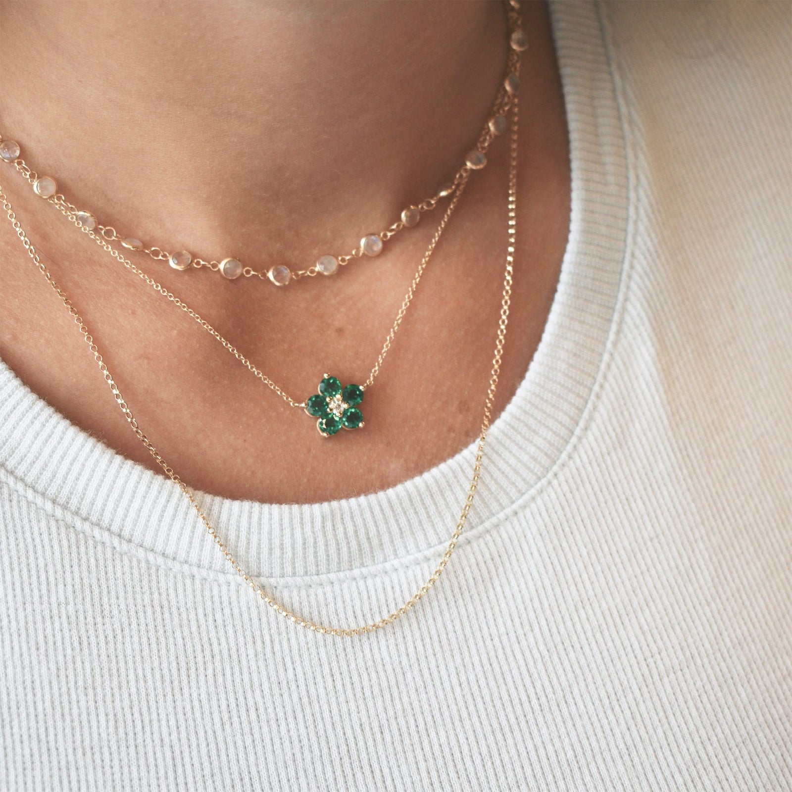 Woman wearing layered 14k gold necklaces including a Greenwich necklace featuring five 4 mm emeralds and one 2.1 mm diamond