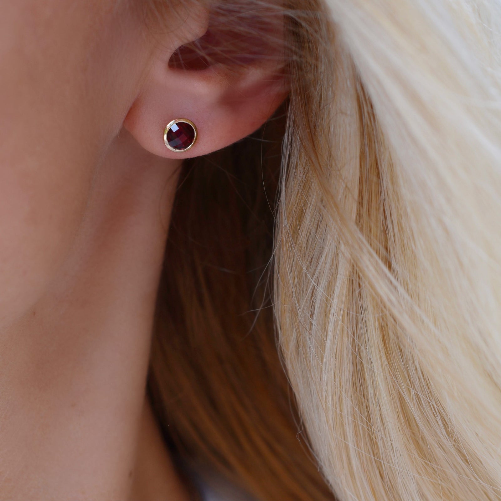 Woman wearing a 14k yellow gold Grand stud earring featuring one 6 mm briolette cut bezel set ruby
