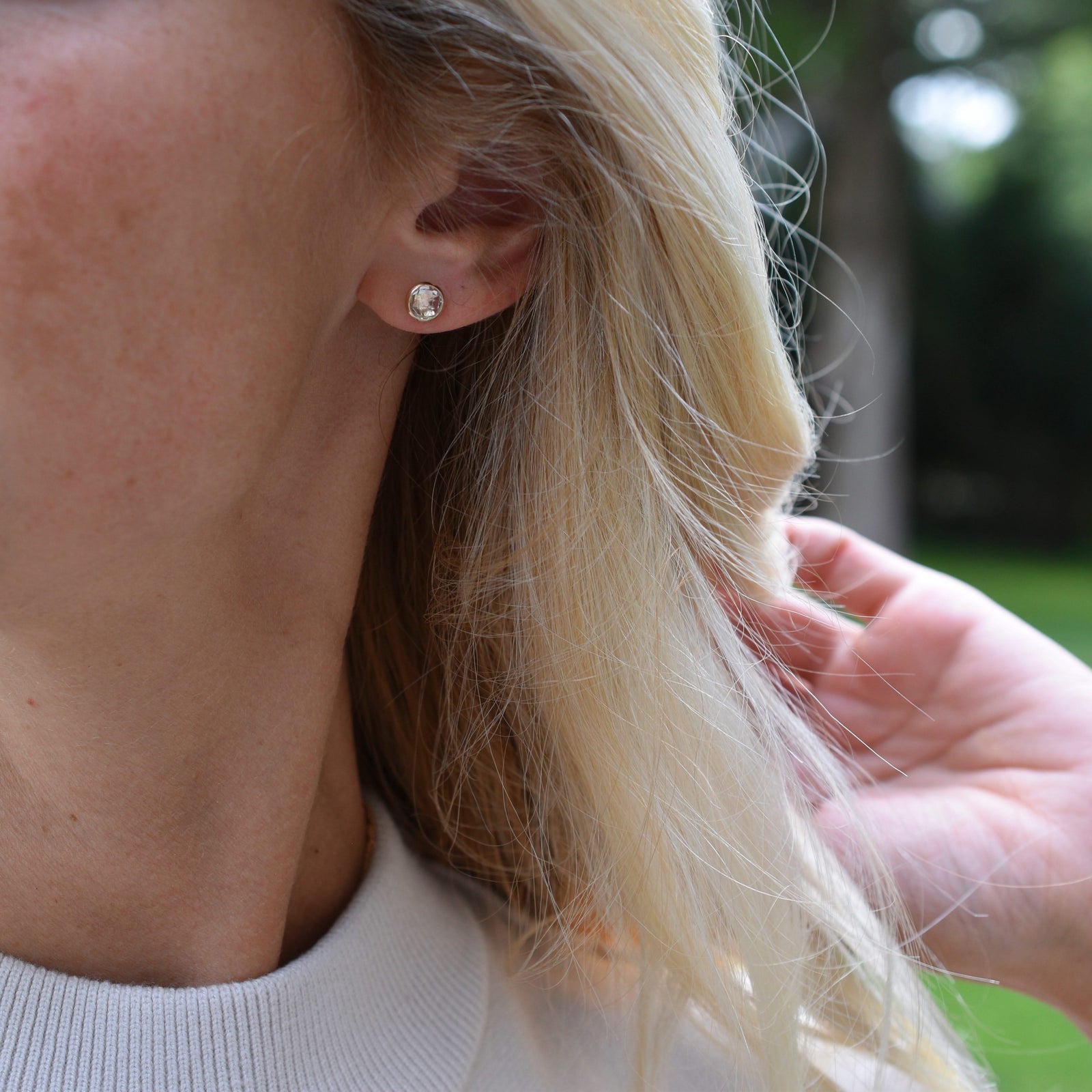 Woman wearing a 14k yellow gold Grand stud earring featuring one 6 mm briolette cut bezel set white topaz