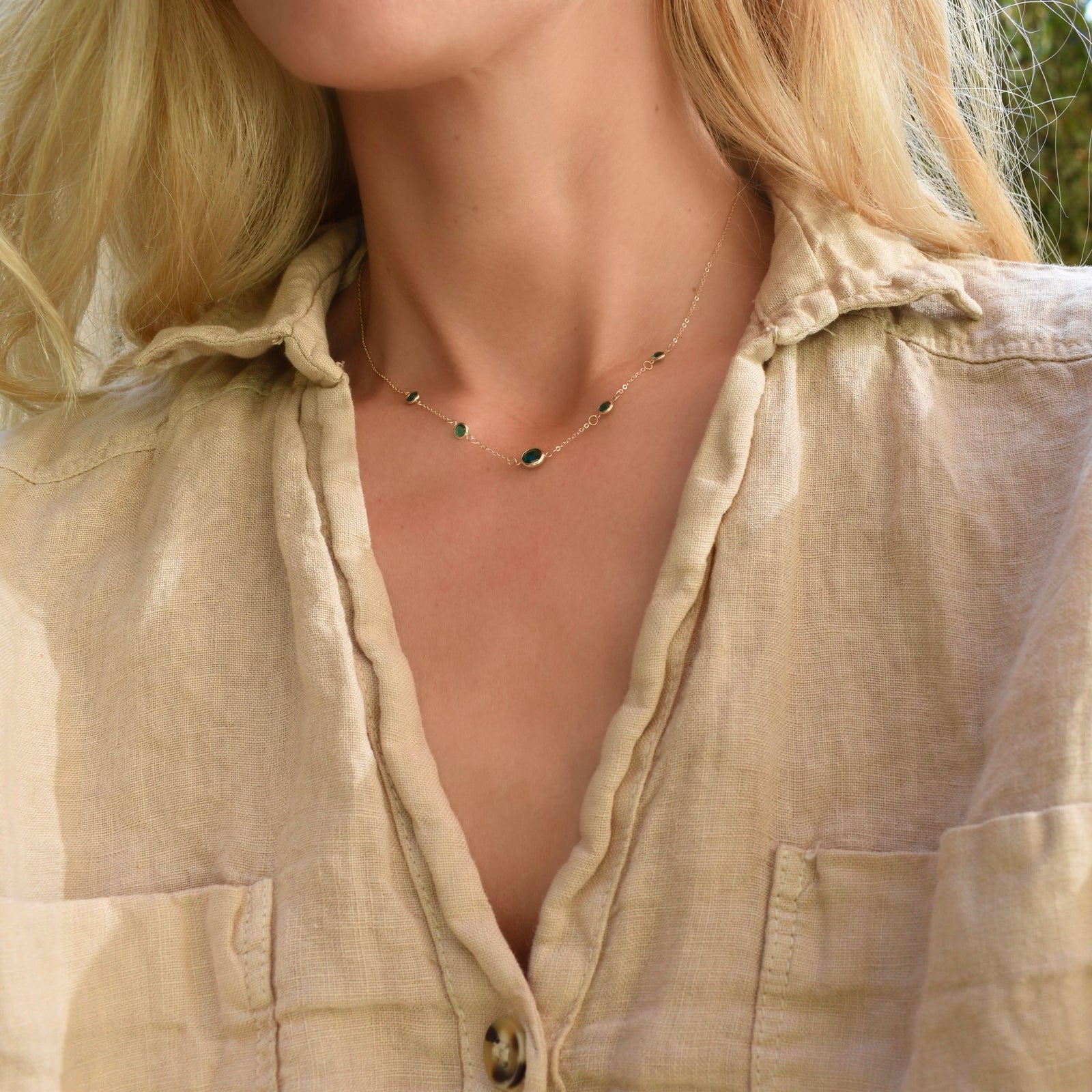 Woman wearing a Grand & Classic necklace featuring one 6 mm and four 4 mm Emeralds bezel set in 14k yellow gold