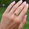 Hand wearing a 1.6 mm wide 14k yellow gold Grand ring featuring one 6 mm briolette cut bezel set ruby