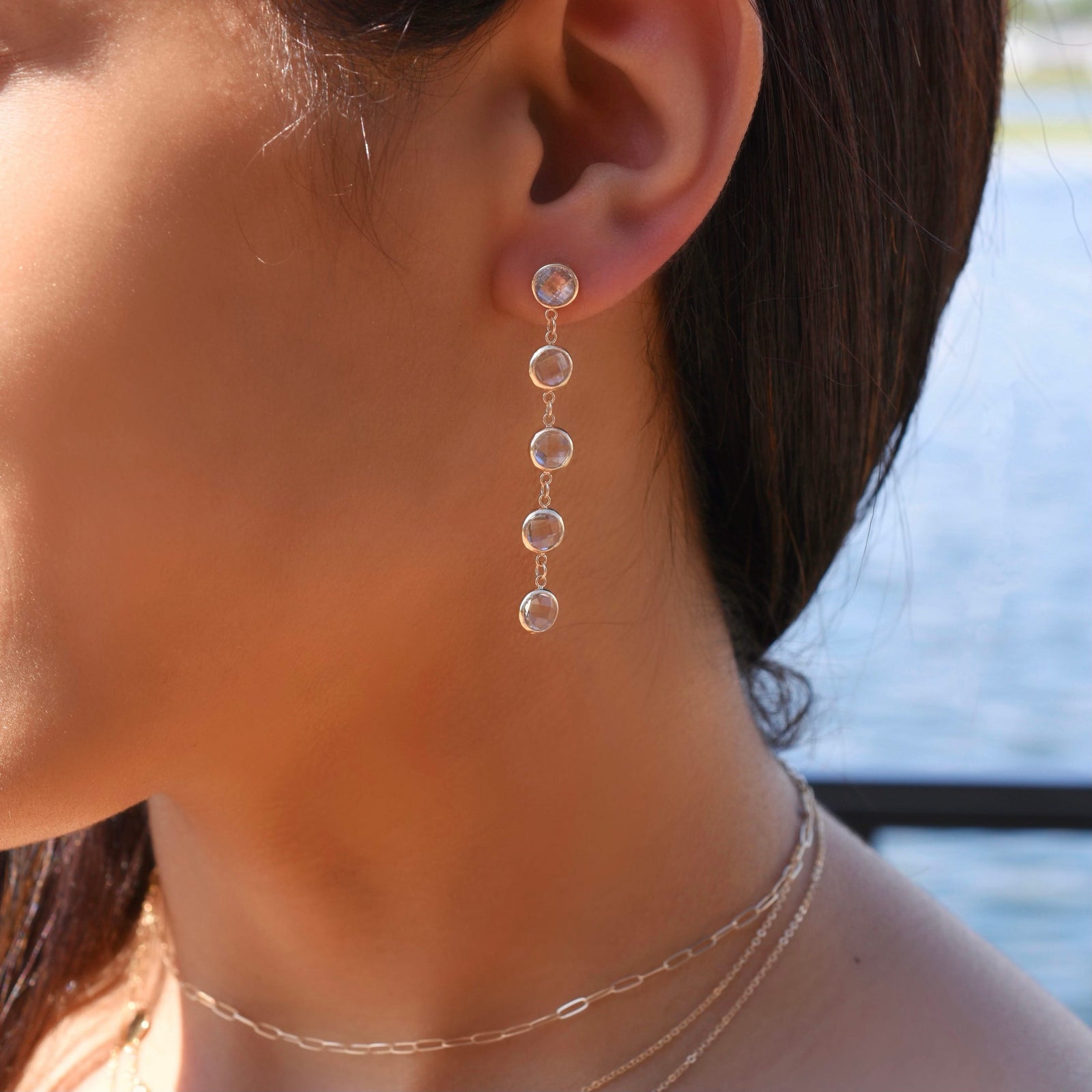 Woman wearing necklaces and a 14k yellow gold Grand stud earring featuring five 6 mm briolette cut bezel set white topaz