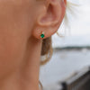 Woman wearing a 14k yellow gold Greenwich 1 Birthstone earring featuring one 4 mm emerald and one 2.1 mm diamond