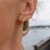 Woman wearing a 14k yellow gold Greenwich 1 Birthstone earring featuring one 4 mm peridot and one 2.1 mm diamond