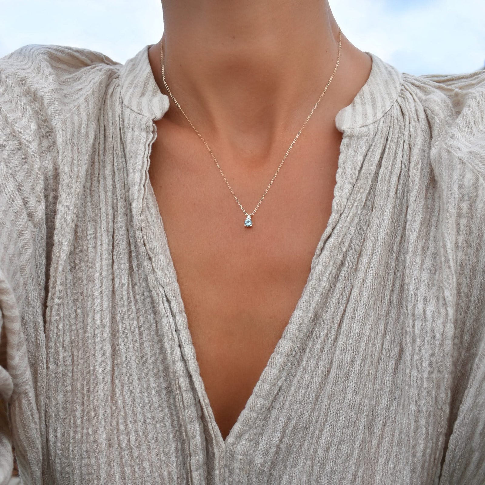 Woman wearing a Greenwich necklace featuring one 4 mm Nantucket blue topaz & one 2.1 mm diamond bezel set in 14k gold