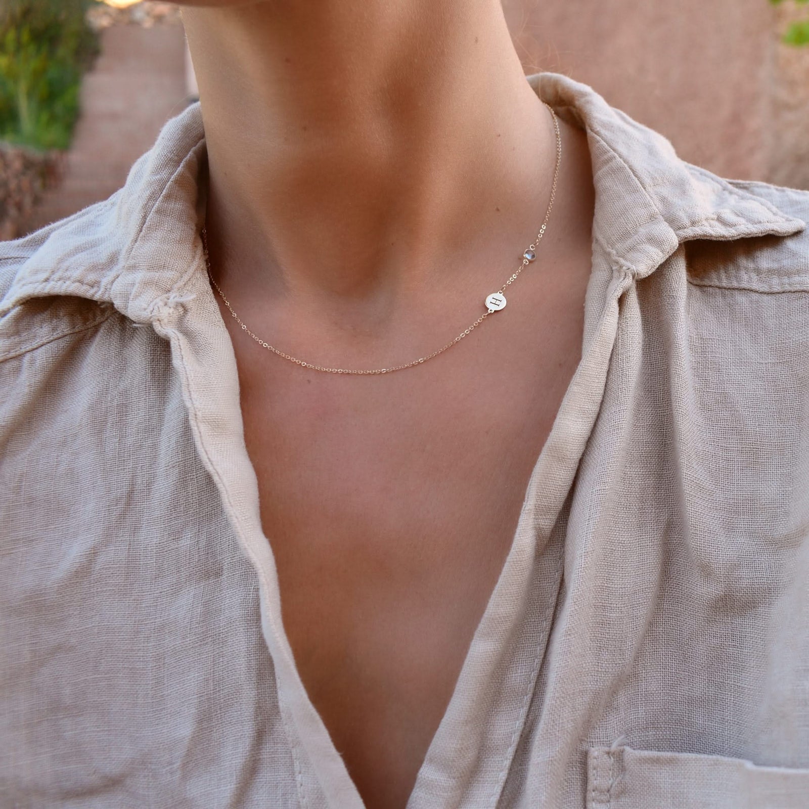 Woman wearing a 14k yellow gold Classic necklace featuring one birthstone and one 1/4” flat disc engraved with the letter H