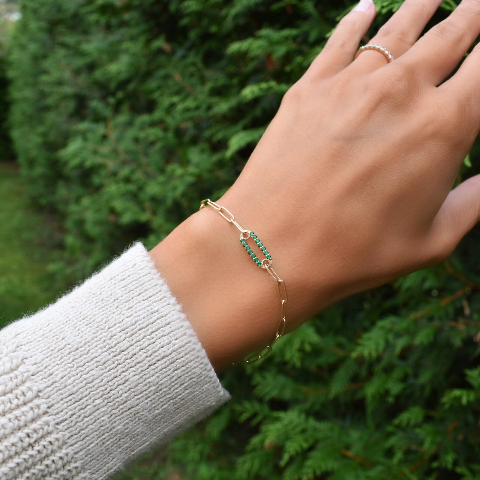 Woman wearing a 14k yellow gold Adelaide paperclip chain pavé bracelet featuring one emerald-encrusted link