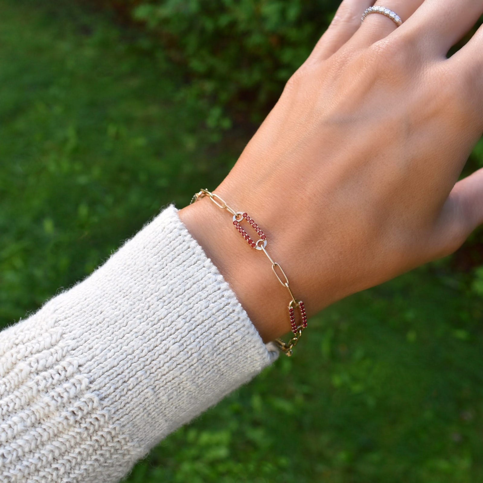 Woman wearing a 14k gold Adelaide paperclip chain pavé bracelet featuring garnet-encrusted links
