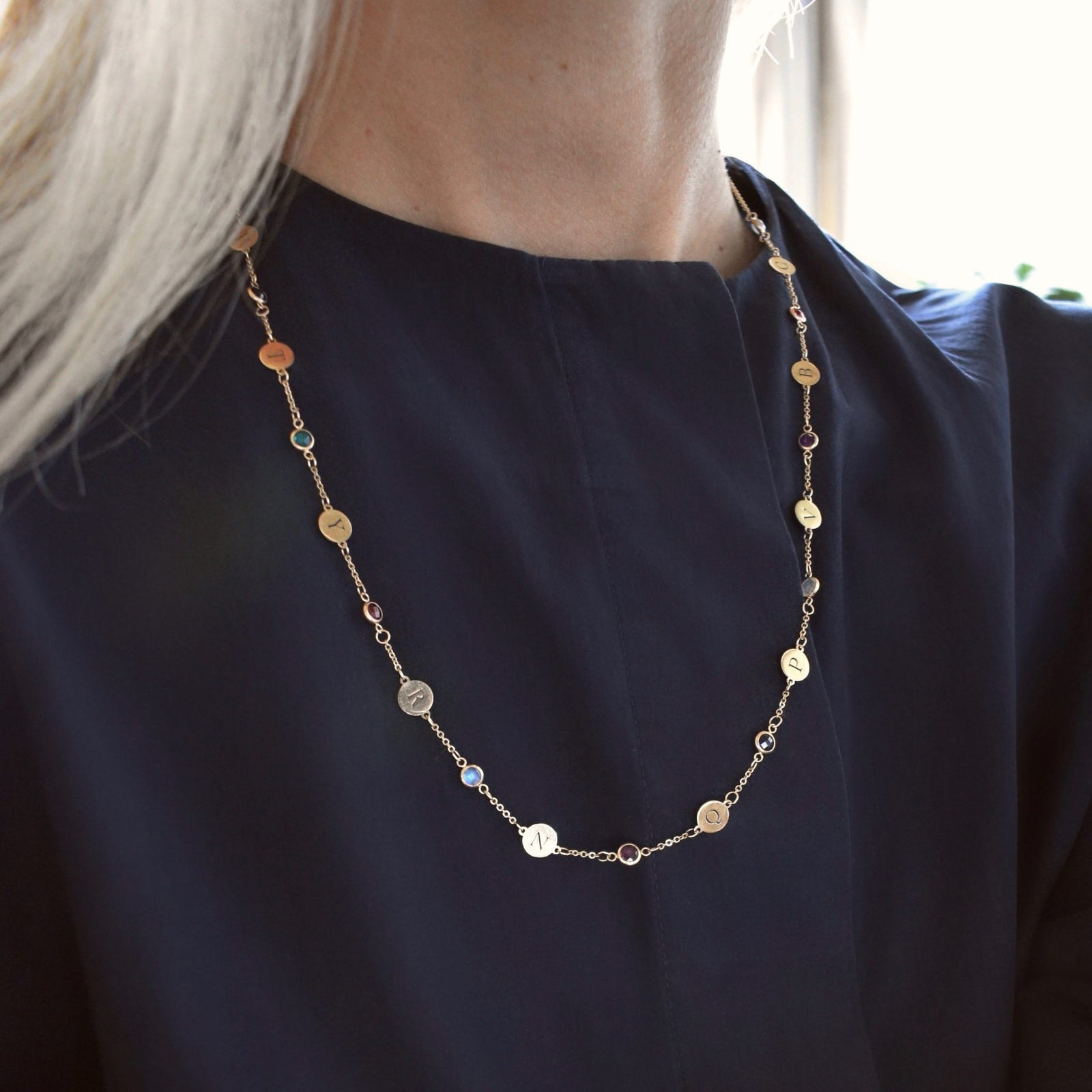 Woman wearing a 14k yellow gold Classic necklace featuring 10 birthstones and 10 flat discs engraved with letters