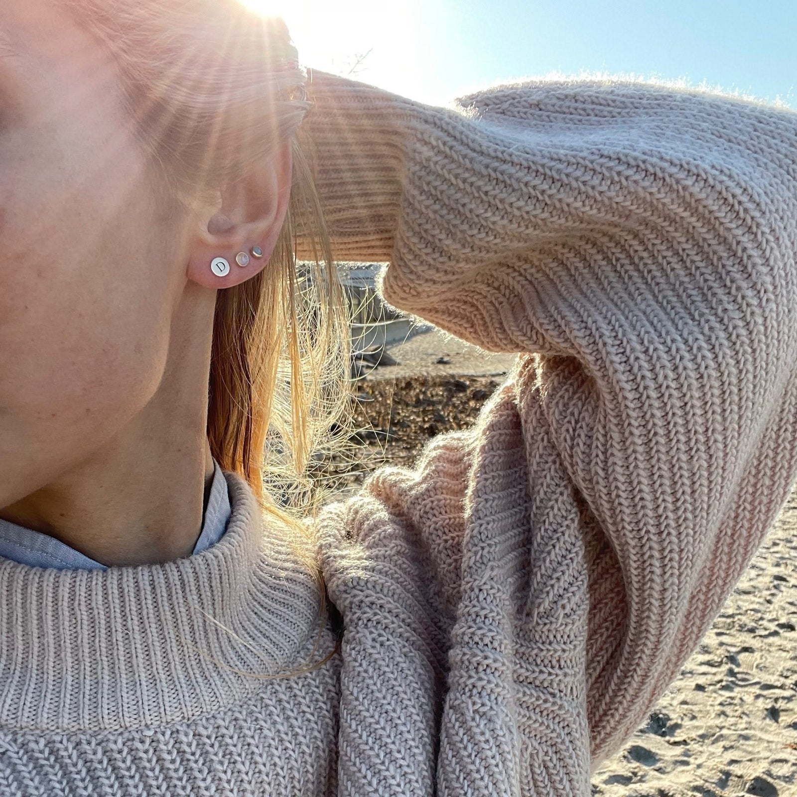 Woman wearing three earrings including a 14k yellow gold stud earring featuring one 1/4” flat disc engraved with the letter D