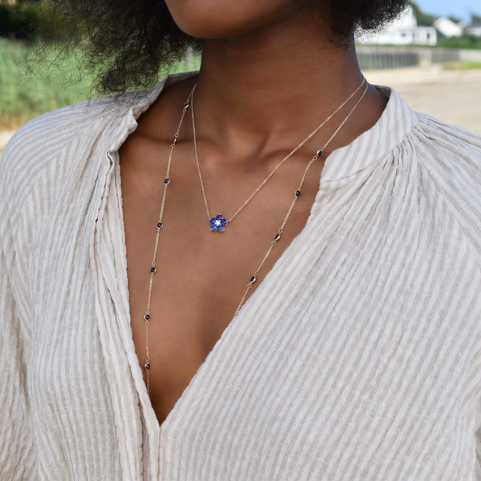 Woman wearing two gold necklaces including a Greenwich necklace featuring five 4 mm round cut sapphires & one 2.1 mm diamond
