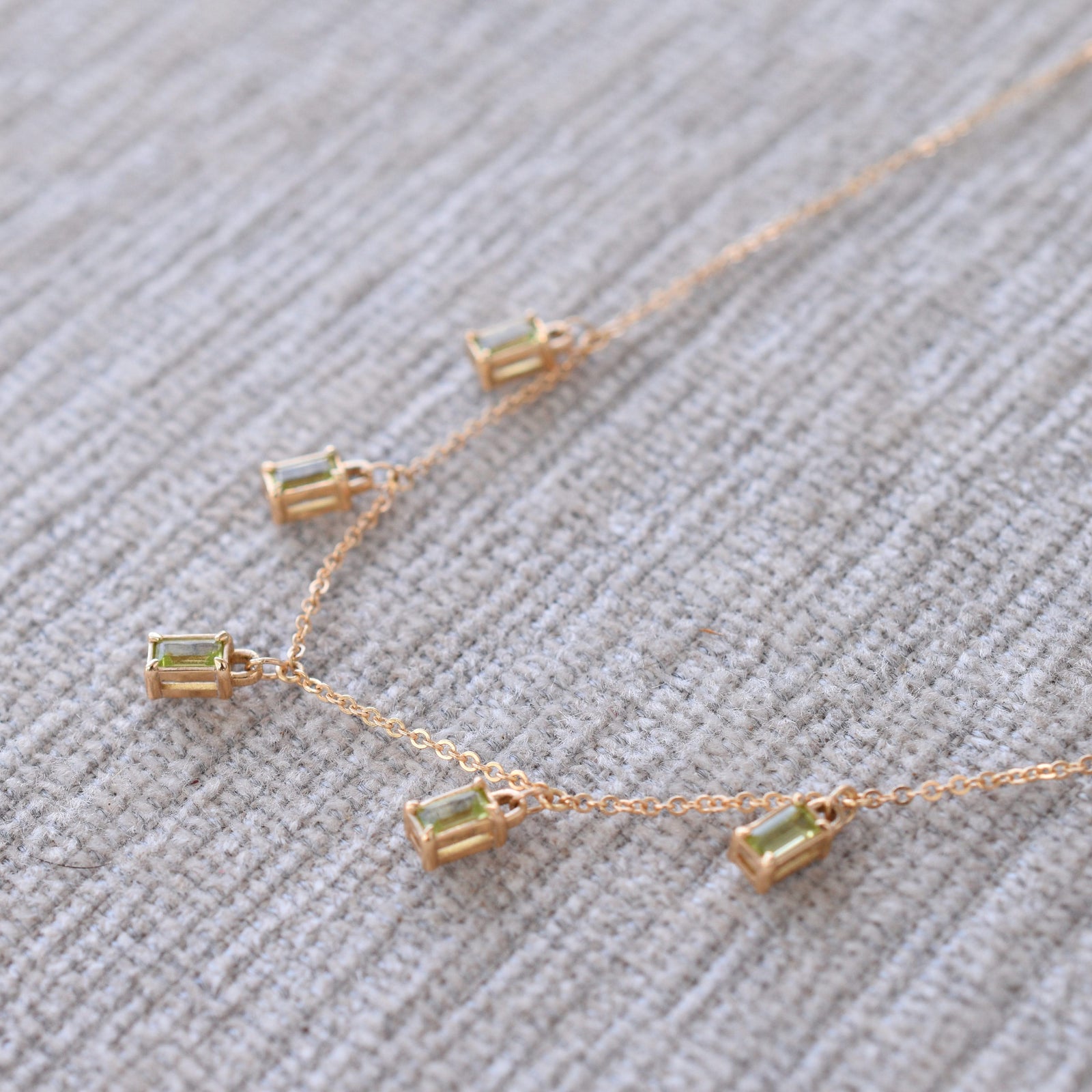 Close-up of a Providence 5 Peridot drop necklace with petite baguette cut stones set in 14k yellow gold