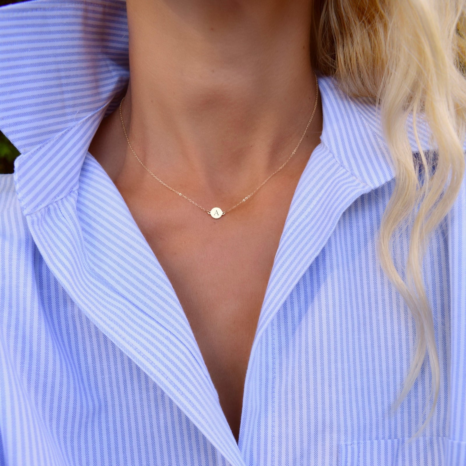 Woman wearing a 14k yellow gold cable chain necklace featuring one 1/4” flat disc engraved with the letter A