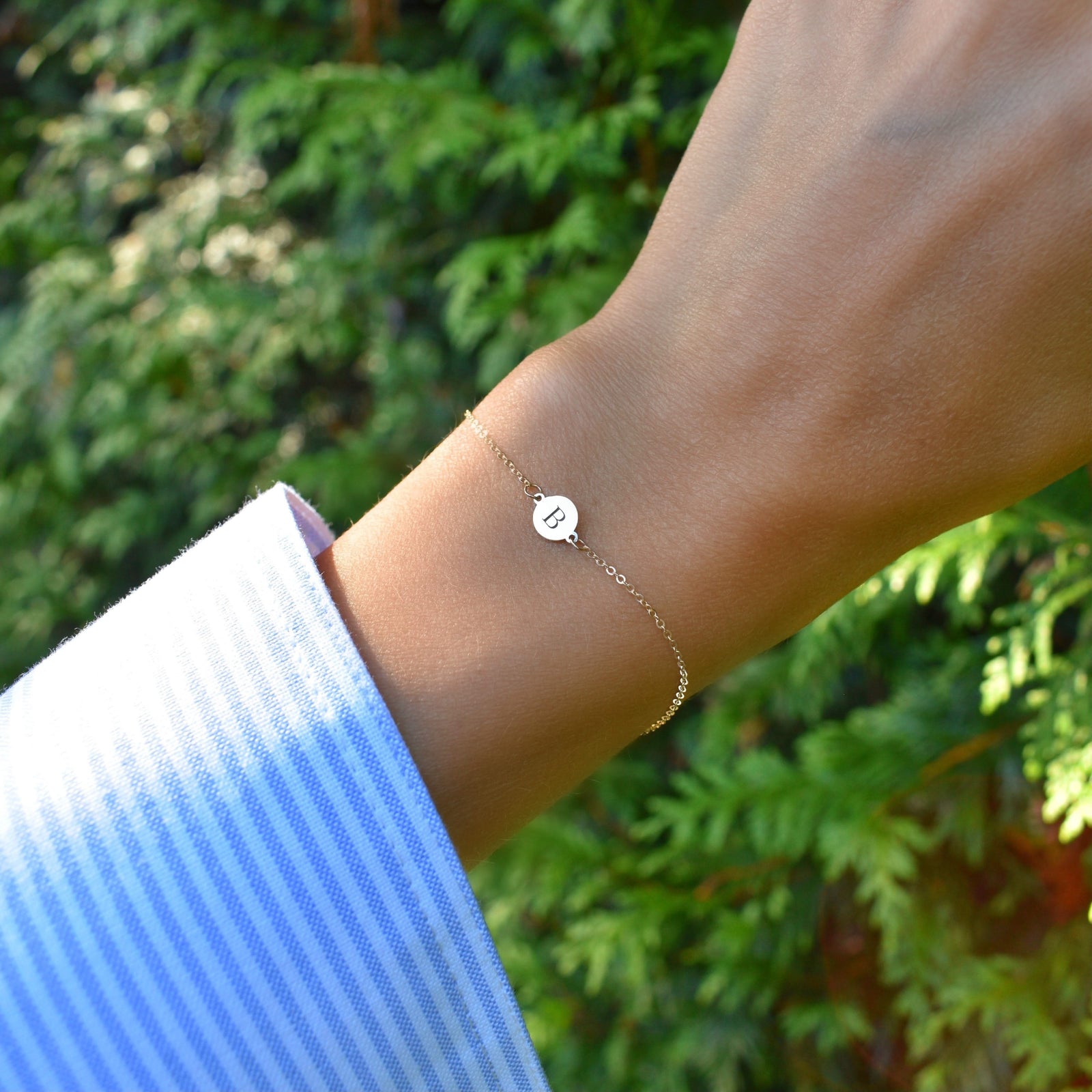 Woman wearing a 14k yellow gold cable chain bracelet featuring one 1/4” flat disc engraved with the letter B