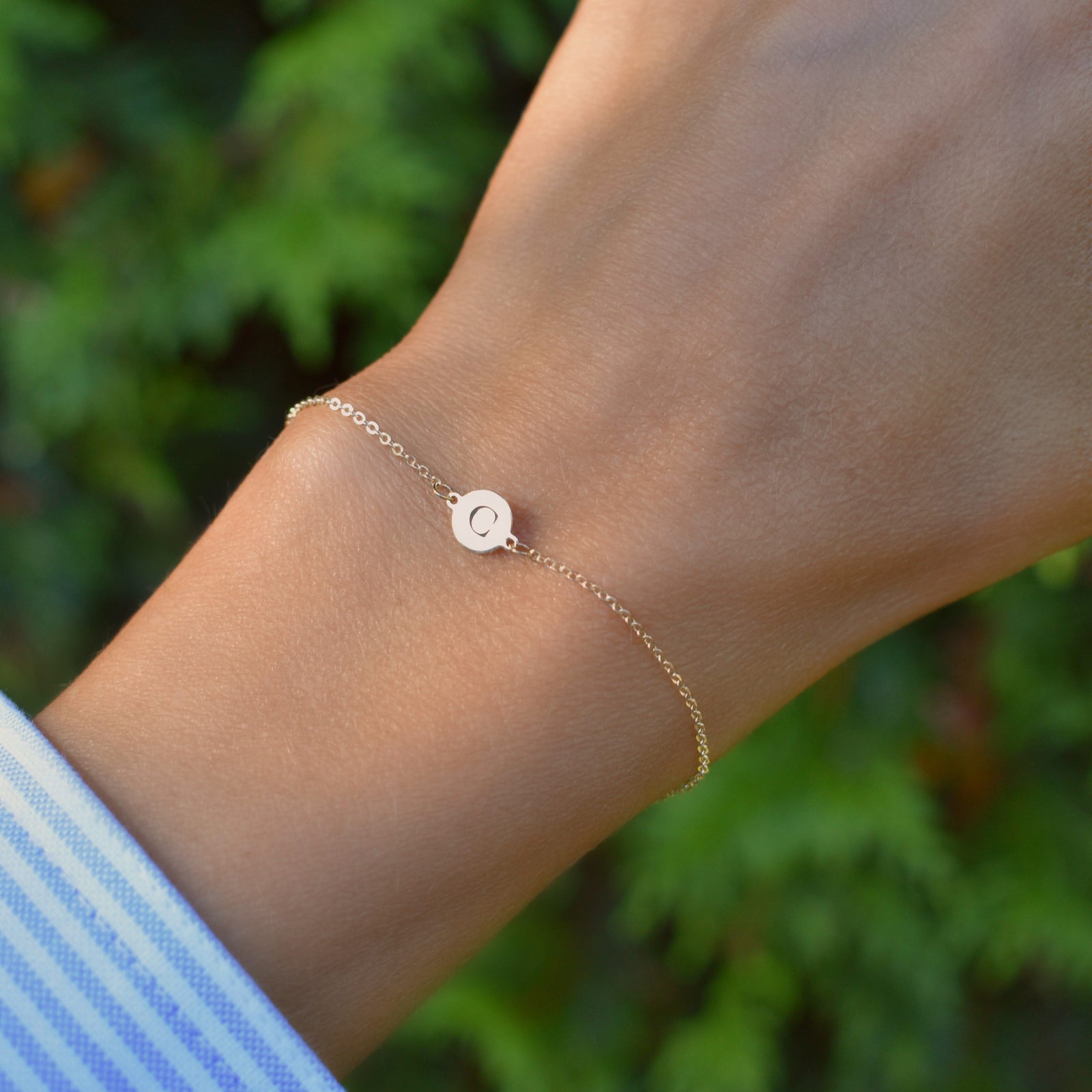 Woman wearing a 14k yellow gold cable chain bracelet featuring one 1/4” flat disc engraved with the letter C