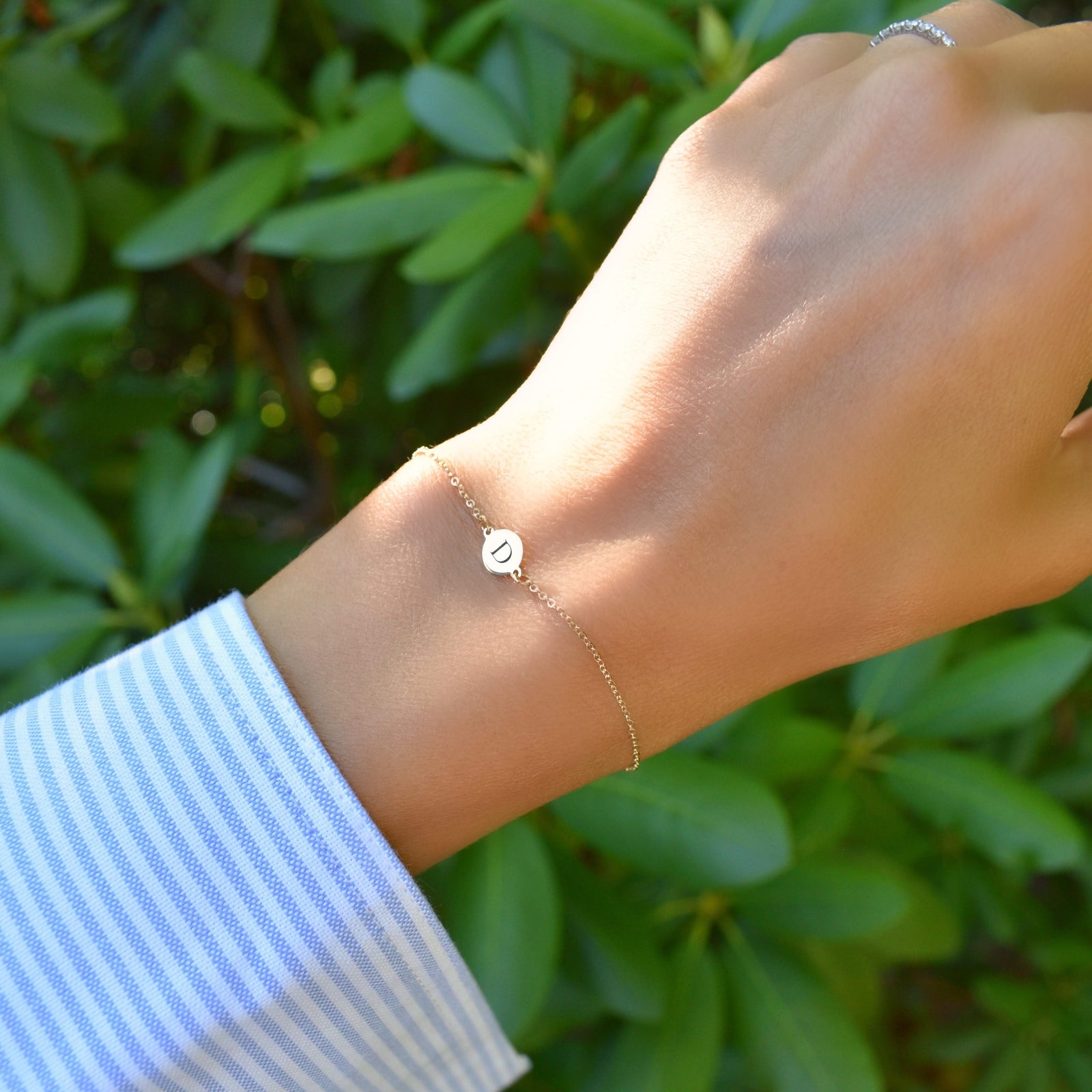 Woman wearing a 14k yellow gold cable chain bracelet featuring one 1/4” flat disc engraved with the letter D